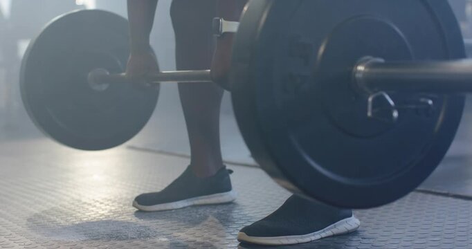 African male training duo bracing gripping and pulling barbell at gym, spotter steadying with watch