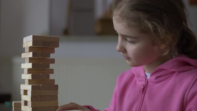 Child Having Fun Building Constructor Tower of Wooden Blocks. Girl Playing Wooden Block Tower Game at Home. Board Creative Game. Child Development Education Leisure. Play With Wooden Building Blocks.