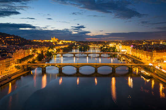 Breathtaking drone panorama of Prague at sunset, featuring Prague Castle and the bridges over the Vltava River under a cloudy evening sky.