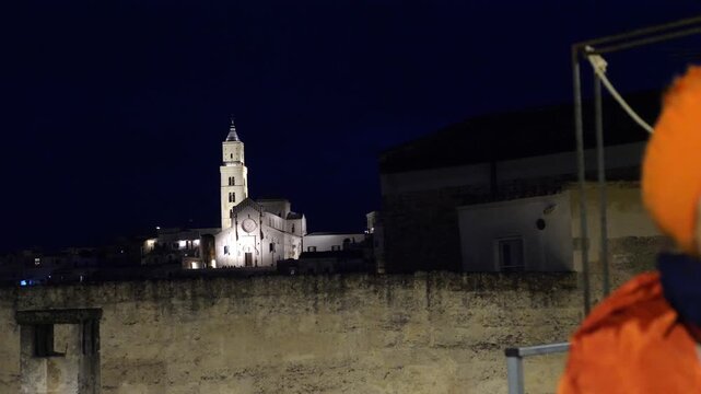 Backward camera movement starting from Cattedrale di Matera and revealing a mature woman in orange jacket smiling in the foreground