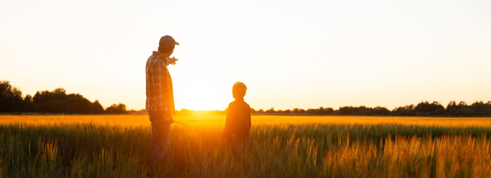 Farmer and his son in front of a sunset agricultural landscape. Man and a boy in a countryside field. Fatherhood, country life, farming and country lifestyle concept.