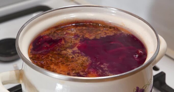 Main first course of Ukrainian cuisine. Ukrainian borscht is cooked on gas stove. Cooking first courses. National dish of Ukraine. Red Ukrainian borscht is boiling in white saucepan, zoom-in video
