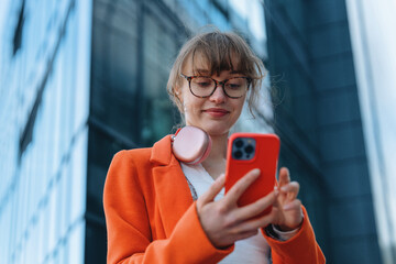 Young woman checks phone while standing near modern office building in city