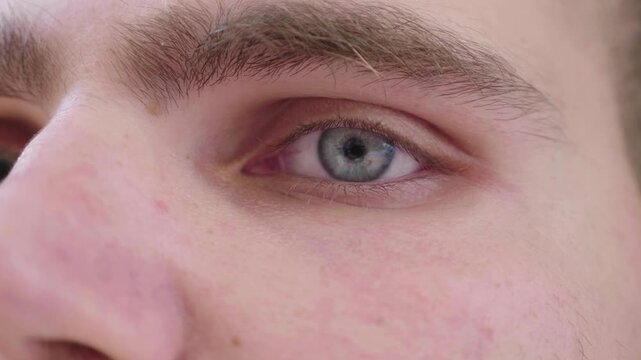 Extreme macro close-up of a blue eye of a young man. Detailed human eye texture and iris pattern highlighting vision, perception and human observation.