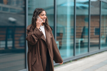 Obraz premium Woman talking on phone while walking near building with glass windows in city