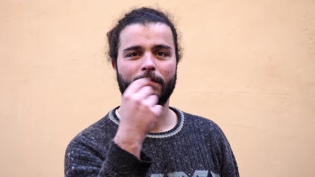 A bearded young man gestures with his hands asking what do you want from me, expressing frustration and confrontation.