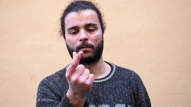 A bearded young man uses his fingers to indicate that something is very small, expressing size comparison through clear hand gestures.