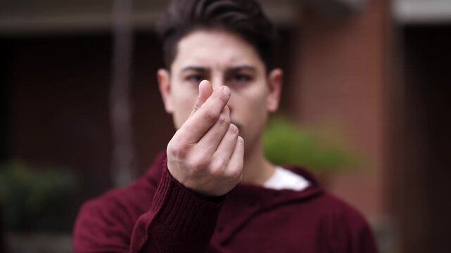 Young man wearing a burgundy sweater gesturing with his hand to ask for money, expressing demand, expectation, and financial request.
