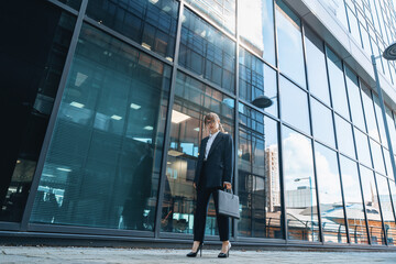 Fototapeta premium Businesswoman walks outside a modern office building holding a briefcase during the day