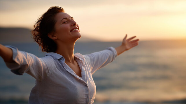 Young woman facing ocean sunset with outstretched arms rejoicing and laughing smiling looking up to sky enjoying life and summer nature connection happiness celebration