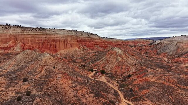 A view of a canyon with steep rocky hills and a dirt path winding through the landscape. The sky is overcast with clouds above the rugged terrain.