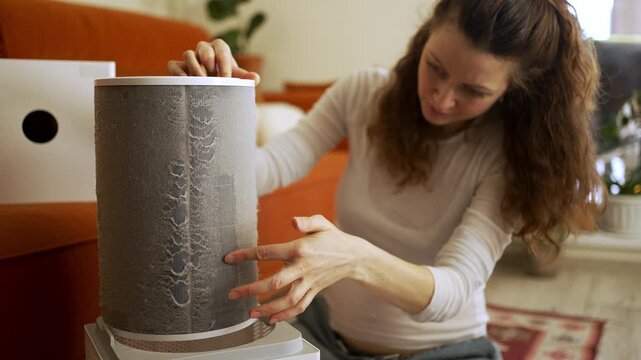 Young woman meticulously cleaning a large layer of dust and dirt from a cylindrical air purifier filter, performing regular maintenance on the appliance for better indoor air quality