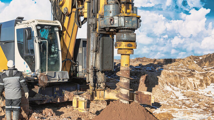 Fototapeta premium A drilling rig is actively working on a pile foundation at a construction site. A worker is present near the rig observing the operation