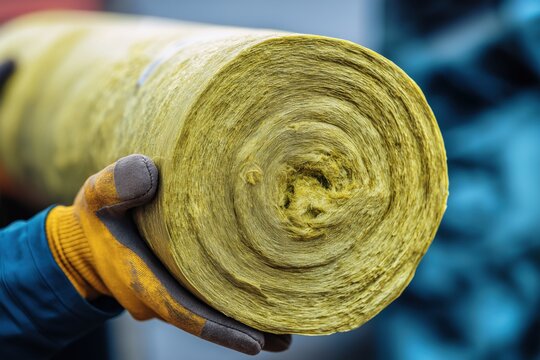 Worker's Gloved Hand Holding a Roll of Yellow Mineral Wool Insulation