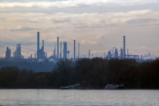 Industrial structures rise above the river in a cloudy setting during the early evening hours