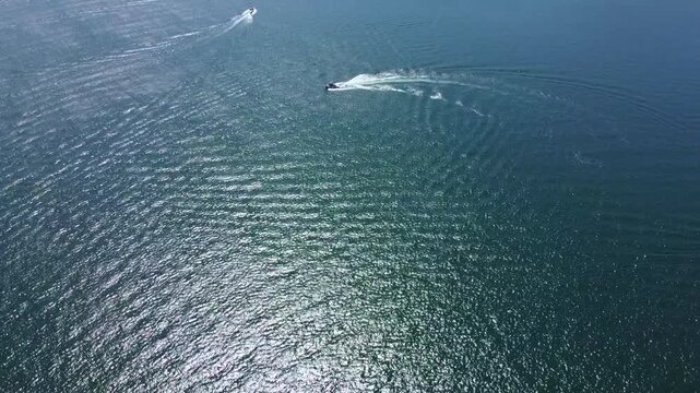 Stunning drone footage of motorboats making turns on a calm lake. Sparkling sun rays reflecting off the deep blue water surface. Adventure, summer vacation, and luxury travel atmosphere.