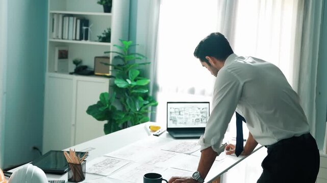 Architect engineer using laptop planning house design at office while sitting at meeting table with blueprint and equipment scatter around.Skilled civil engineer working at blueprint. Alimentation.