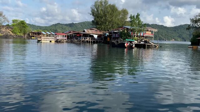 Traditional Bajo tribe stilt houses built over crystal clear sea water. Scenic coastal village of sea gypsies with green hills and blue sky reflections in Central Sulawesi, Indonesia.