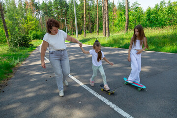 Obraz premium Active happy grandmother and granddaughters having fun time together skateboard in the forest.