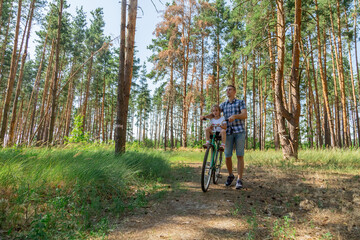Obraz premium Dad rides his daughter in a bicycle seat in forest. A man carries a small child on a bicycle.