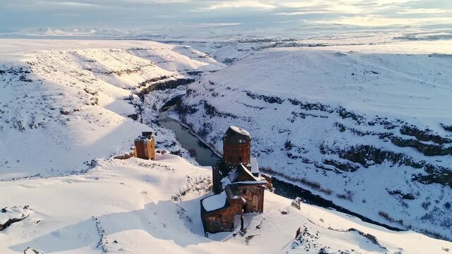 Aerial view of the Menucehr Mosque minaret at Ani Ruins overlooking a snowy canyon in Kars, Turkey. Medieval stone architecture rises above a dramatic winter landscape.