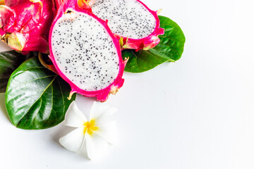 Tropical dragon fruits - pitahaya - with frangipani flower and green leaves on white table