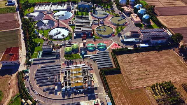 A water treatment facility shows multiple circular tanks and solar panels. Surrounding farmland is visible with patches of green and brown fields.