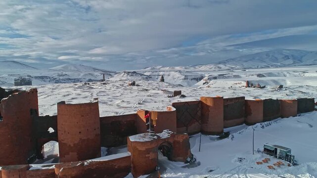Aerial view of the medieval city walls of Ani in Kars, Turkey. Snow covered defensive towers and stone fortifications stand against a vast winter landscape.