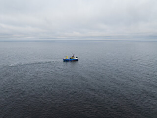 Obraz premium Aerial drone view of a blue commercial fishing vessel pulling a large net in the open waters of the Baltic Sea.