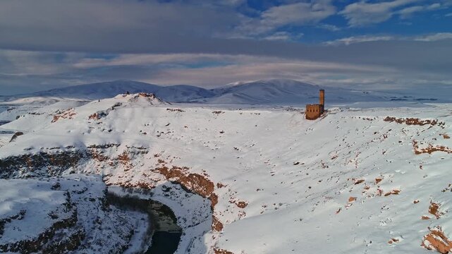 Aerial view of the Menucehr Mosque minaret at Ani Ruins overlooking a snowy canyon in Kars, Turkey. Medieval stone architecture rises above a dramatic winter landscape.