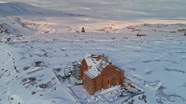 Aerial view of Ani Cathedral and Menucehr Mosque minaret at Ani Ruins in Kars, Turkey. Snow covered medieval structures stretch across the vast Anatolian winter landscape.