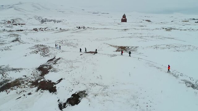 Aerial view of tourists exploring Ani Ruins in Kars, Turkey during winter. Snow covered medieval Armenian city near the border, historic churches, cultural heritage and travel destination.