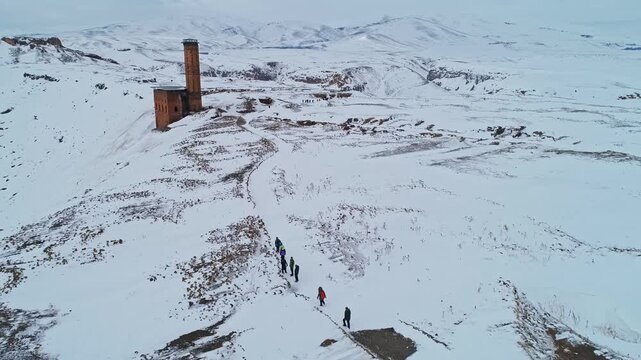 Aerial view of tourists exploring Ani Ruins in Kars, Turkey during winter. Snow covered medieval Armenian city near the border, historic churches, cultural heritage and travel destination.