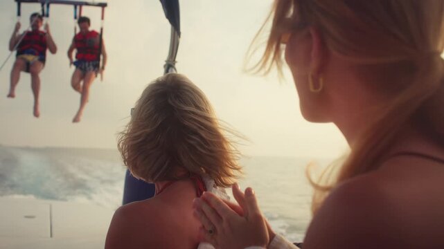People cheering as friends parasail across the open ocean during golden hour