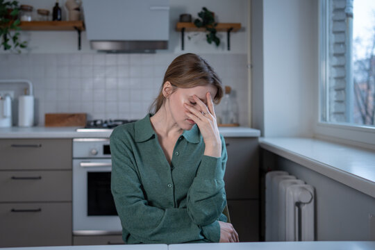 Weary woman sits at kitchen table feels fatigue low energy cover face with hand. Sleepy tired female touching head with tension. Exhausted by stress woman nervously closed eyes with emotional burnout