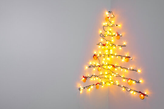 Minimalist sustainable Christmas tree made of string lights and dried orange slices on a white wall corner, zero waste festive interior design concept