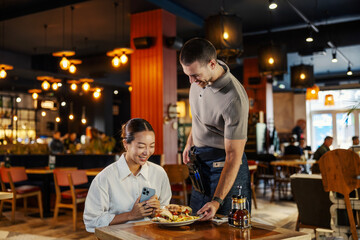 Woman taking food photo in restaurant with waiter serving