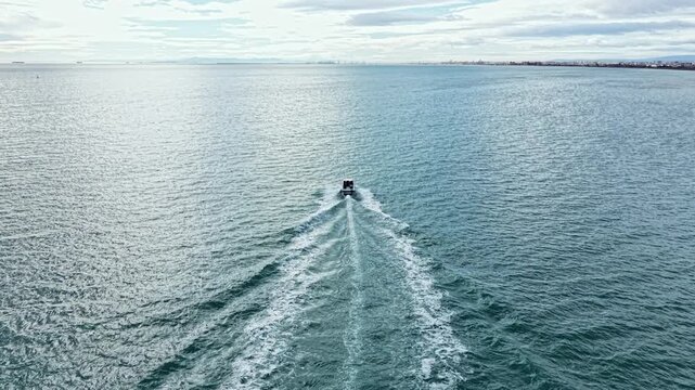A boat travels on the water with a visible trail. The sky is cloudy and the ocean reflects light. This scene shows a simple view of sea travel in the afternoon.