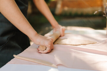 Girl prepares the clay for sculpting, enjoying the artistry and craftsmanship that define traditional pottery. Young woman in an apron gently rolls out clay at outdoor pottery workshop.