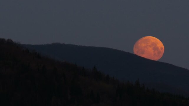 Big orange full moon setting behind mountains