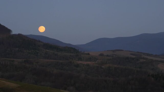 Full moon setting behind a mountain range at dawn
