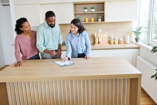 Female Real Estate Agent Selling Modern Apartment To His Young Clients , a couple signing agreement contract in the kitchen In The Fancy Apartment