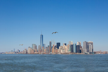 Obraz premium Panoramic view of Lower Manhattan skyline featuring One World Trade Center and waterfront under clear blue sky in New York City.