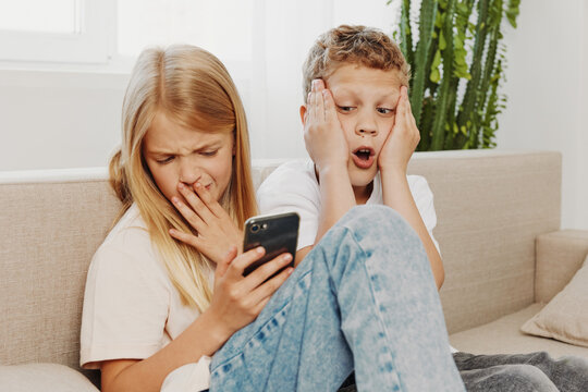 Two children sitting on a couch express shock and disgust while looking at a smartphone screen. Concept of digital content reaction, childhood curiosity, and social media impact.