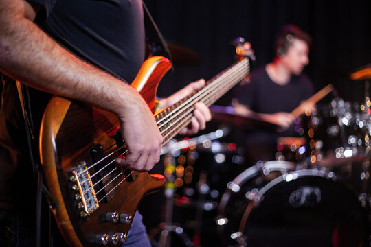 Baixista tocando contra-baixo em est&uacute;dio, baterista desfocado ao fundo