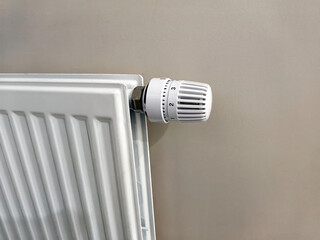 White radiator with a temperature control valve mounted on a beige wall, showcasing a modern heating system in a residential interior setting