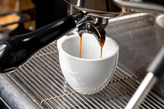 Double stream of espresso pouring into white cup. Close up of hot coffee extraction from portafilter into white ceramic cup on metal grate.