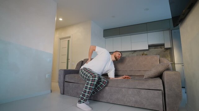 Young man suffering from acute back pain getting up from sofa