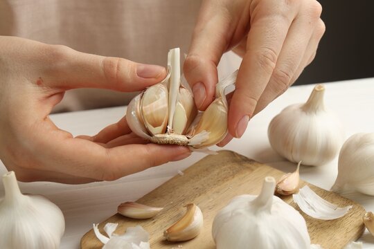 Woman peeling fresh garlic at white wooden table, closeup