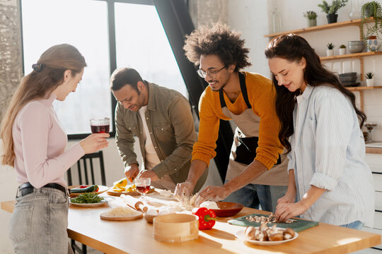 Diverse friends cooking together in kitchen enjoying food preparation and socializing